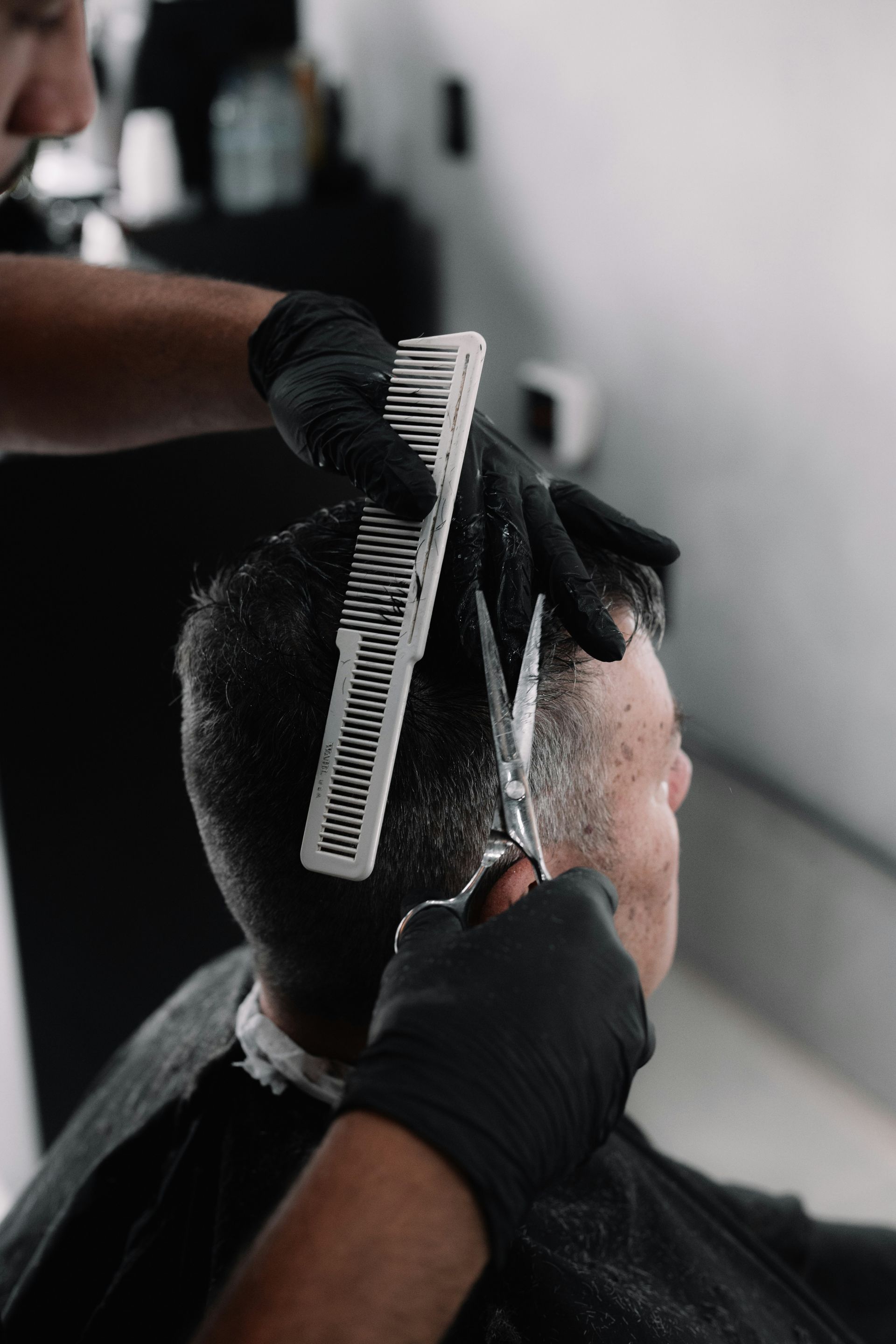 A barber in black gloves cutting a man's hair